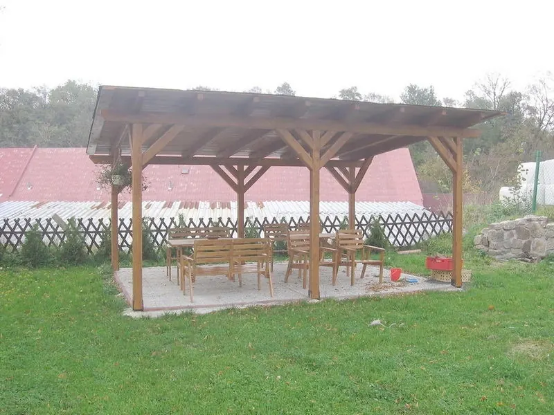 Dřevěná pergola se stoly na trávníku u penzionu